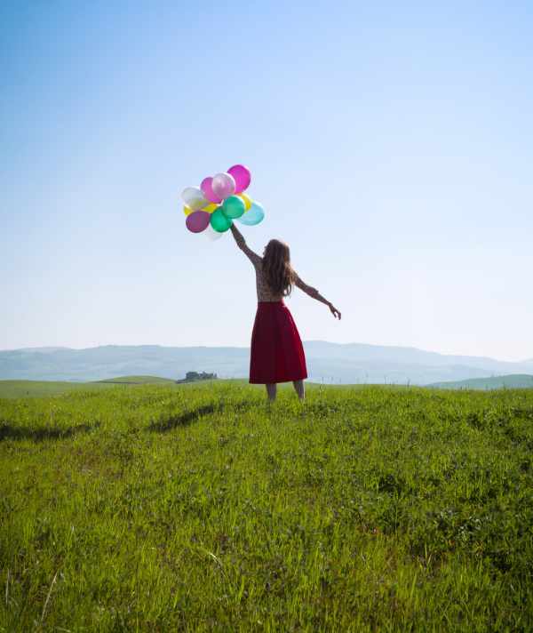 Happy girl in the meadows tuscan with colorful balloons, against the blue sky and green meadow. Tuscany, Italy