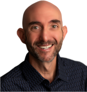 A headshot of handsome Mike Garrett, the curator of Spin Positive. He is shot from the shoulders up. He is a white, bald man with a stubble beard and dark eyebrows. He looks directly at the camera smiling while wearing a dark button down shirt.