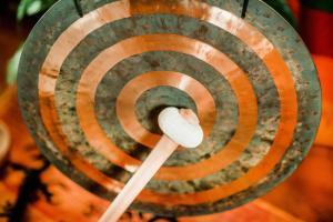 A bronze gong with concentric rings along its face is struck with a white tipped wooden mallet.