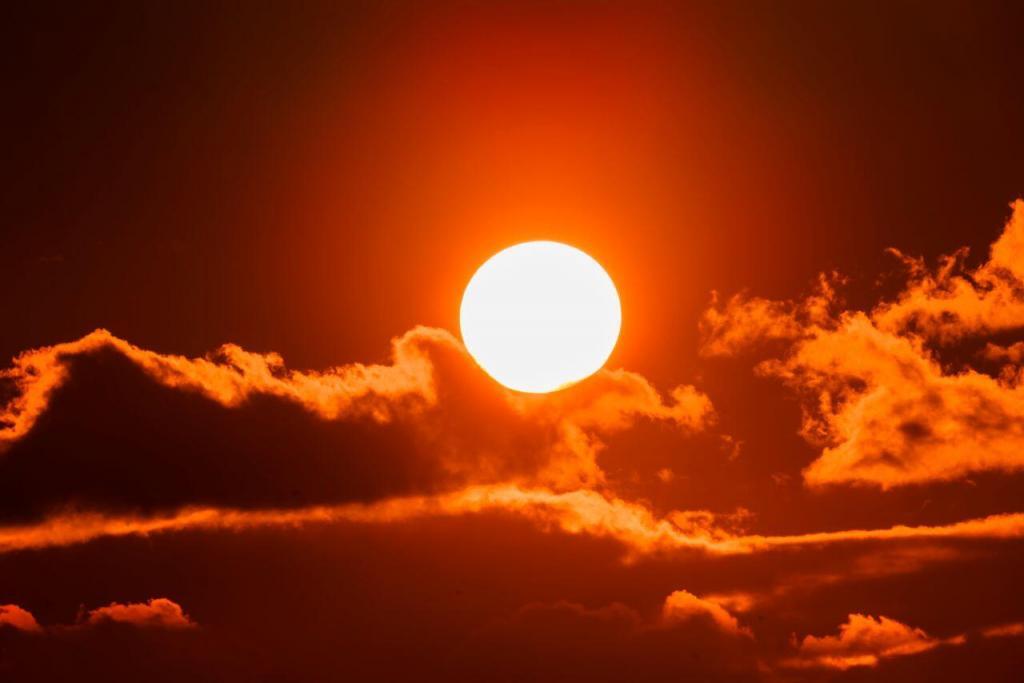 A bright, yet subdued sun blazes in the center of the picture in bright yellow. Just behind and around is a darker sky and under, wispy clouds float shamelessly by